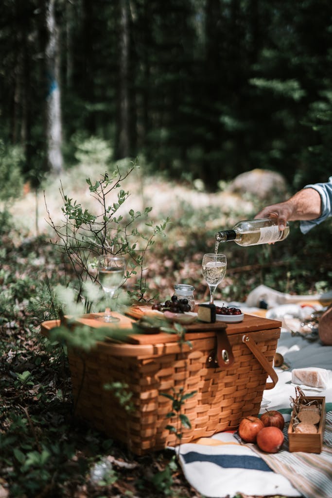 A serene picnic setup in the woods with wine being poured, surrounded by nature.