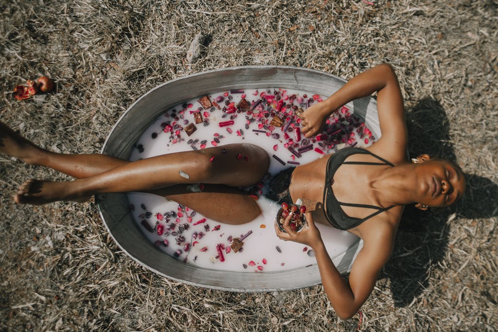 A woman enjoys a tranquil floral milk bath outdoors, promoting wellness and relaxation.